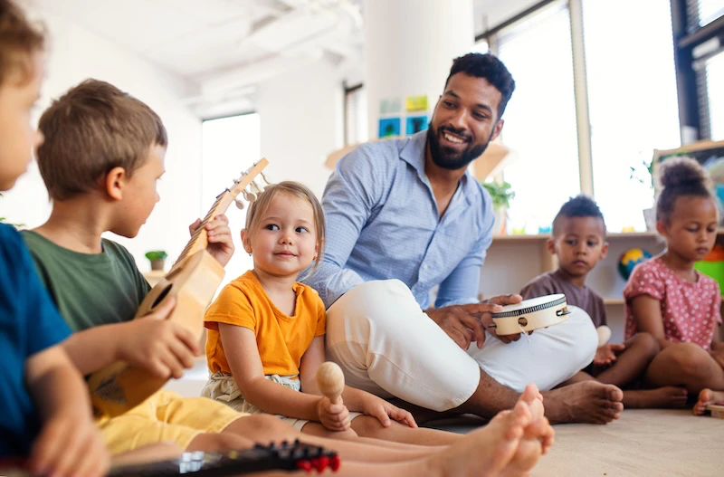 Kids learning and playing with musical instruments with a male instructor in a classroom setting.