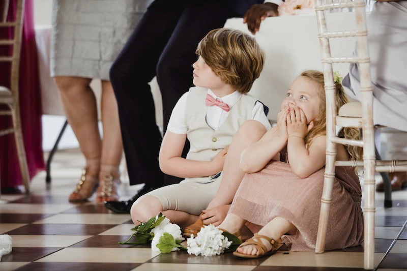 Two young children dressed up and sitting on the floor at a wedding or fancy event.