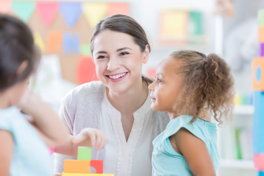 Smiling young woman in a childcare setting with young children.