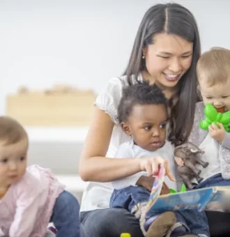 A young woman reading a board book to young toddlers.