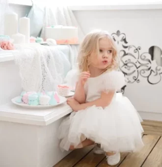 A little blond girl in a white dress with tasty treats.